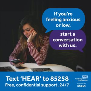 Woman using her phone in a dark room. Text bubbles say: If you're feeling anxious or low, start a conversation with us. White text on a blue banner reads: Text HEAR to 85258 Free confidential support 24/7. NHS Peterborough and Cambridgeshire, and in partnership with shout logos are on the bottom right corner.